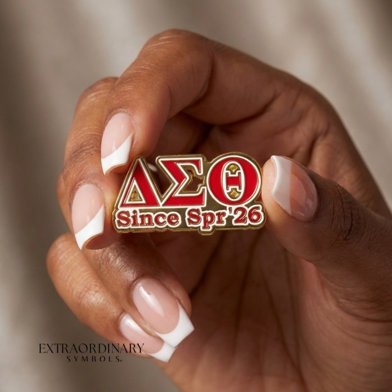 Hand holding a Delta Sigma Theta pin with 'Since Spr '26' text against a neutral background. Crossing gift